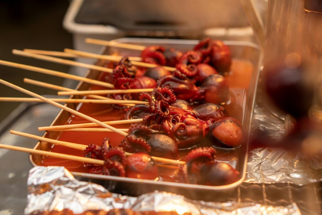 Close-up of skewered tako tamago, a popular Japanese street food, glistening with sauce in a food tray.