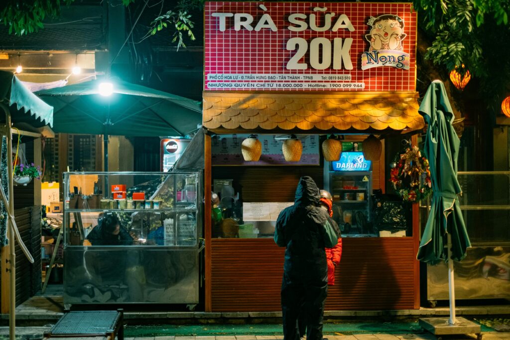 Nighttime street market scene with people buying tea at a cozy outdoor shop.