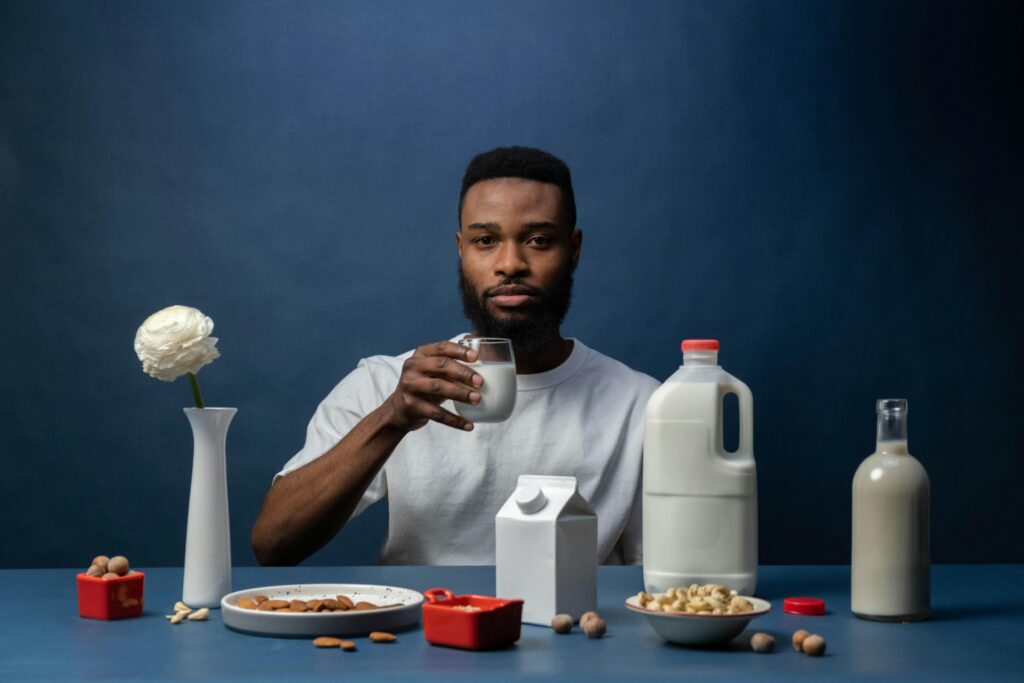 Man enjoying almond milk with a healthy breakfast setup featuring nuts and milk containers.