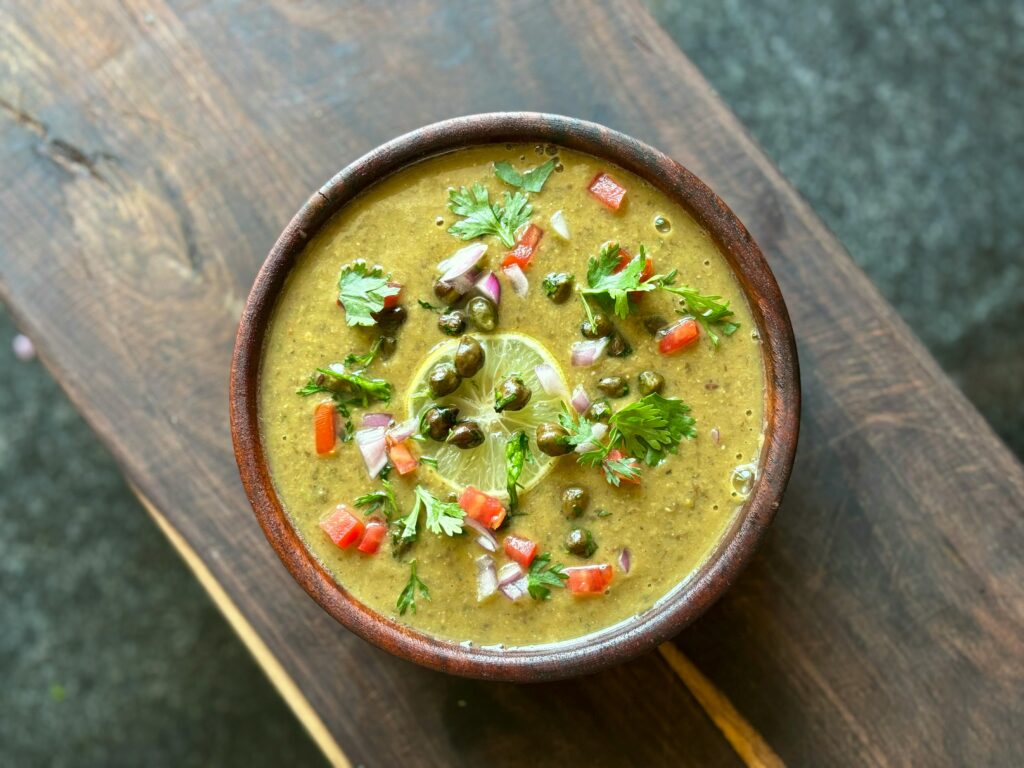A vibrant bowl of traditional Indian lentil soup garnished with fresh coriander, chili, and lime.