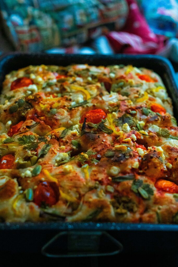 Focaccia bread topped with cherry tomatoes, herbs, and seeds in a baking tray.
