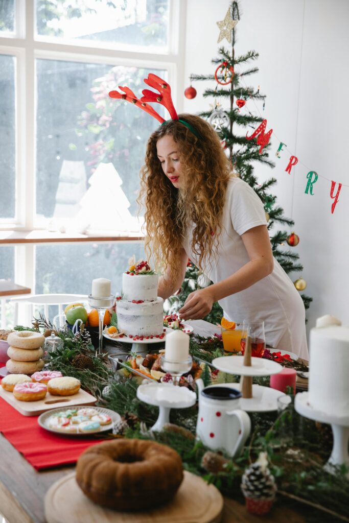 Woman in festive attire arranging holiday baked goods on a decorated table indoors.