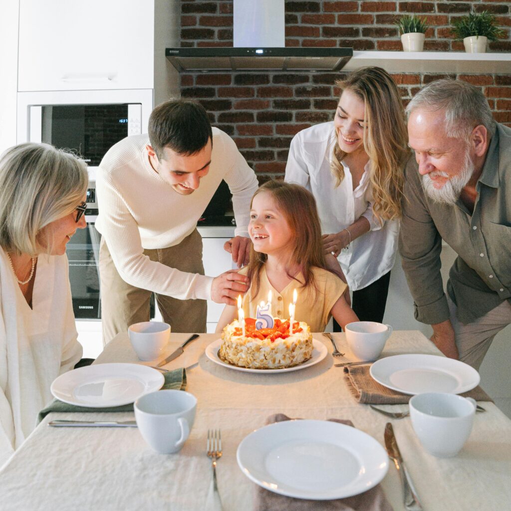 Family gathered indoors celebrating a young girl's birthday with cake and smiles.